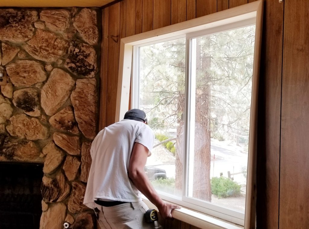 A man installing a window into a home with a wooden interior for higher window efficiency ratings.