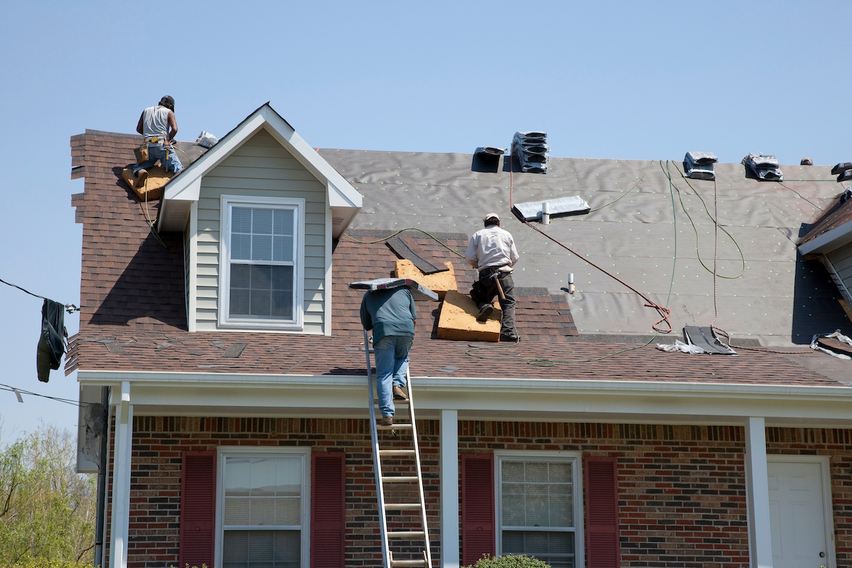 : 3 workers fixing the roof of a two-story home.