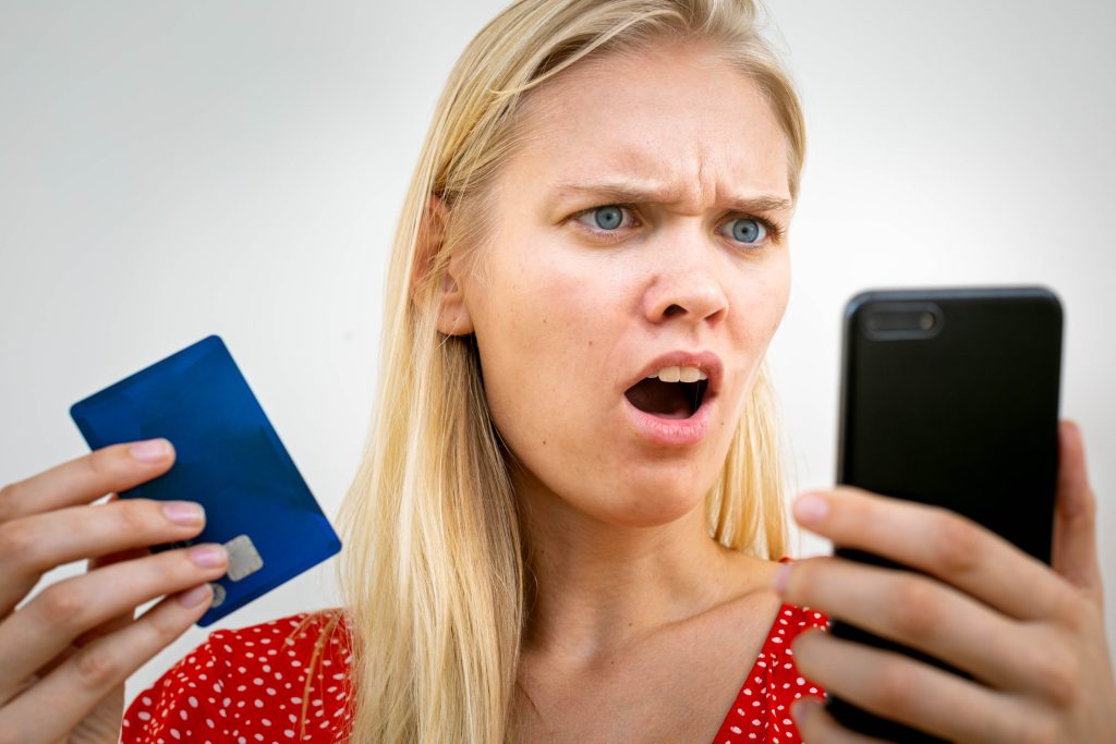 A blonde hair and blue-eyed woman holding a credit card and looking at her phone in shock. What is the best way to finance home improvements with bad credit?