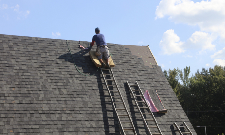 A man on a ladder makes repairs to a roof.