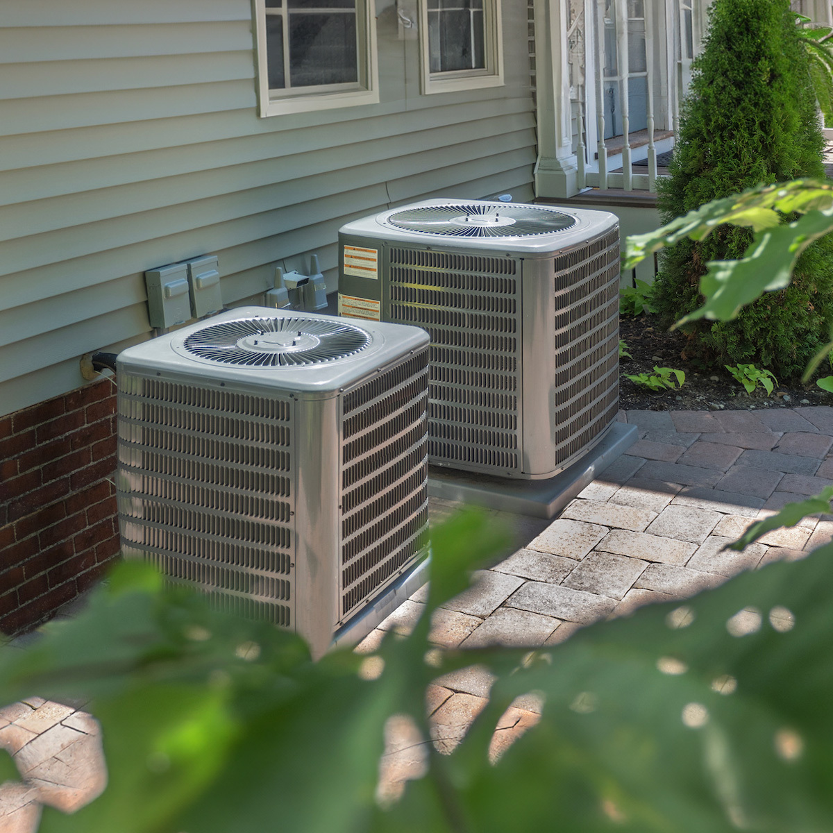 Two outdoor AC units next to one another on a brick floor.
