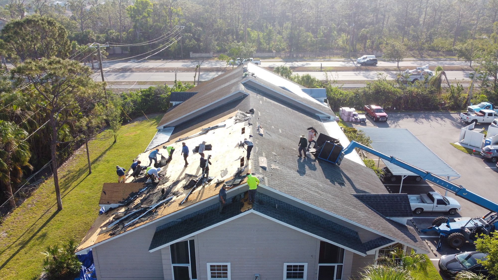 Aerial view of multiple workers repairing a damaged roof on a residential building, with debris around, in Fort Myers, FL, after Hurricane Ian.