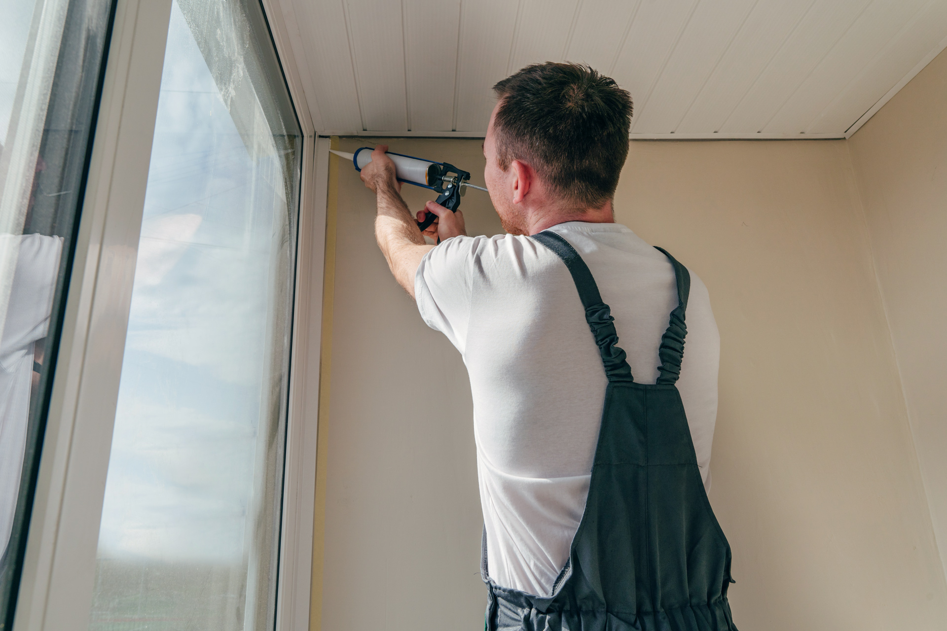 Man in overalls applying caulk to a door.