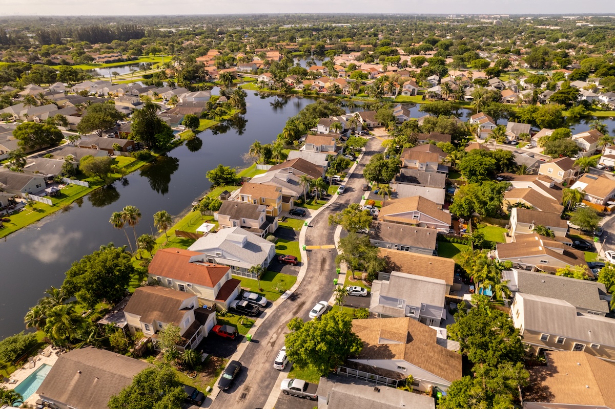 Aerial view of a suburban neighborhood with houses, streets, and water bodies.