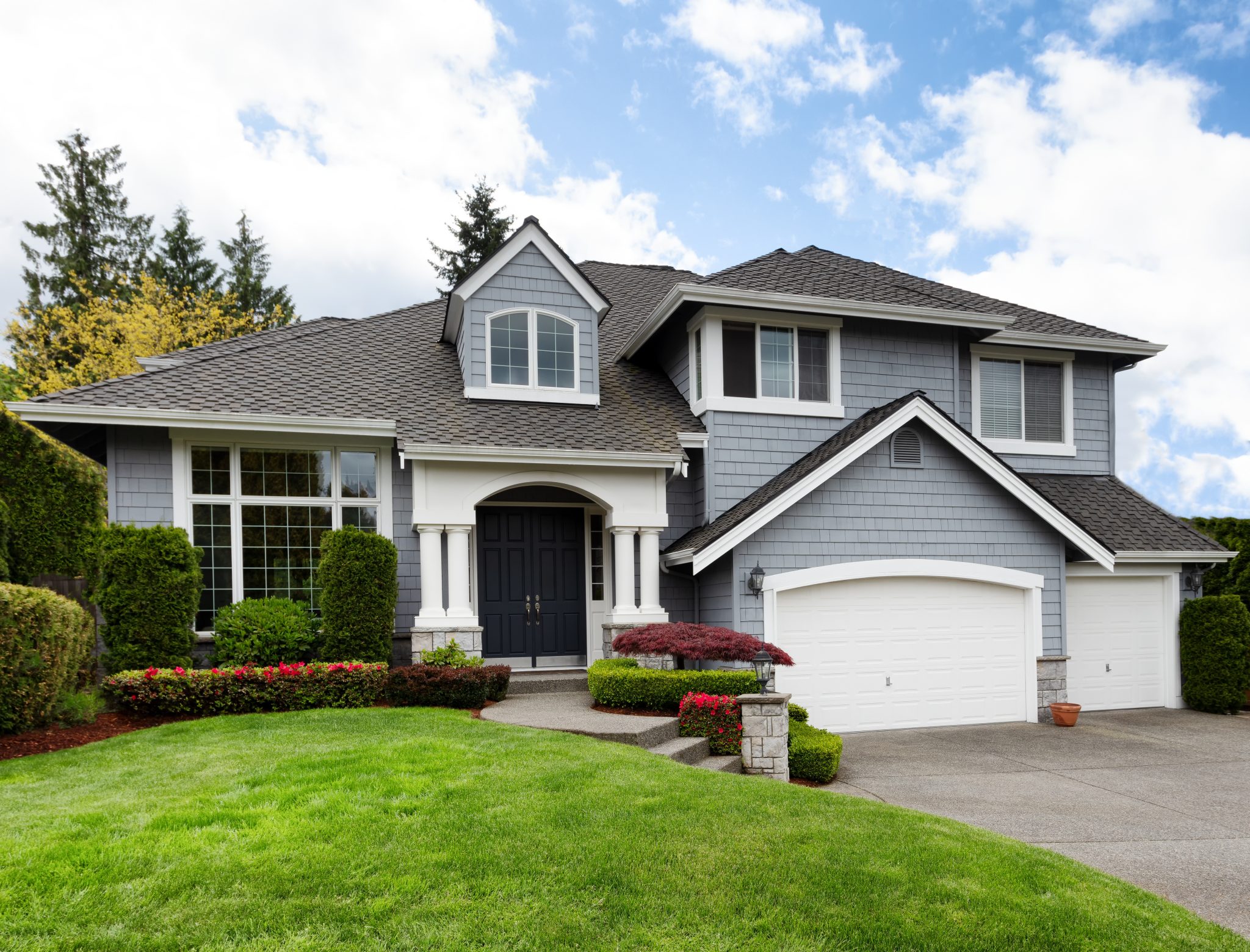 A modern suburban home with gray siding and white trim, featuring a well-manicured lawn, a three-car garage, and a neatly landscaped front yard.